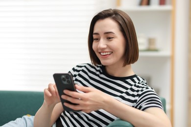 Photo of Woman using modern smartphone on sofa at home