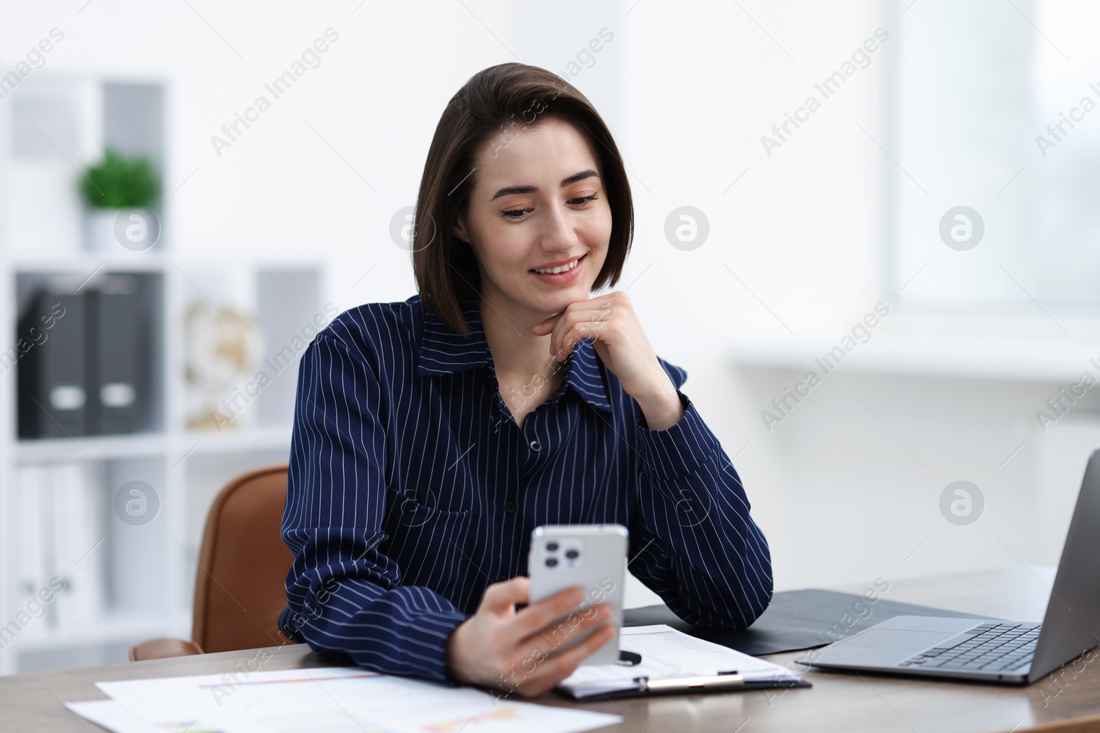 Beautiful woman using her smartphone while working at desk in office Photo of Beautiful woman using her smartphone while working at desk in office