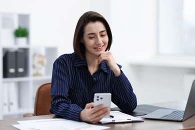 Photo of Beautiful woman using her smartphone while working at desk in office