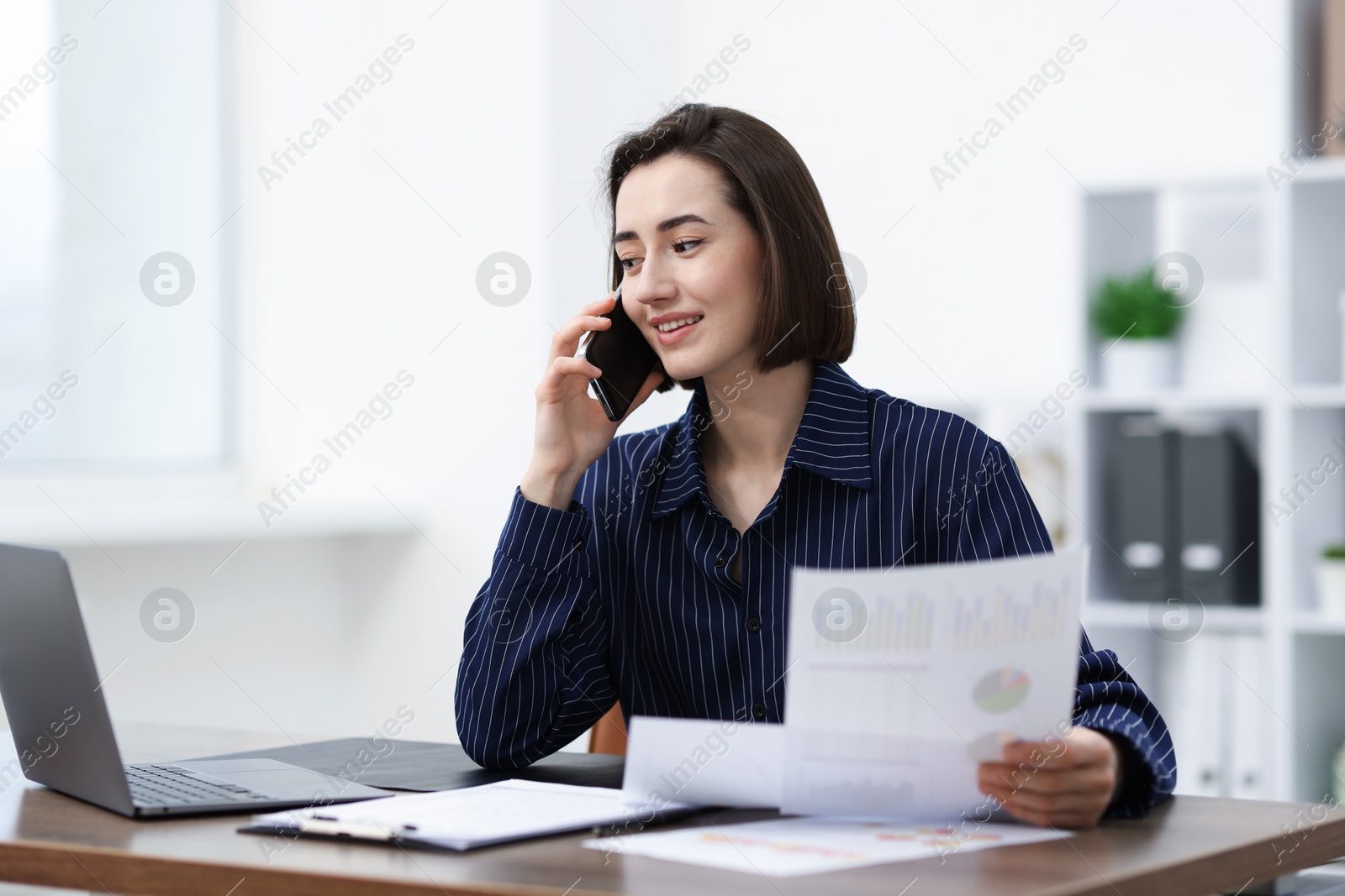 Beautiful woman talking on phone at desk in office Photo of Beautiful woman talking on phone at desk in office