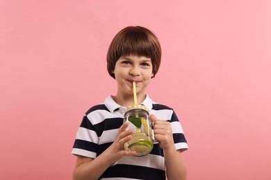 Photo of Cute little boy drinking lemonade on pink background. Refreshing drink