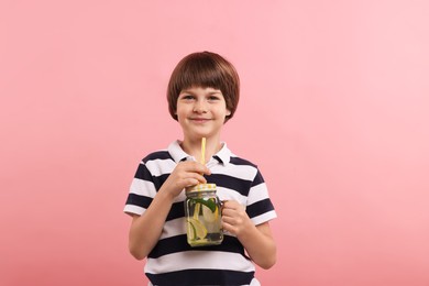 Photo of Cute little boy with mason jar of lemonade on pink background. Refreshing drink