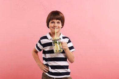 Photo of Cute little boy with mason jar of lemonade on pink background. Refreshing drink