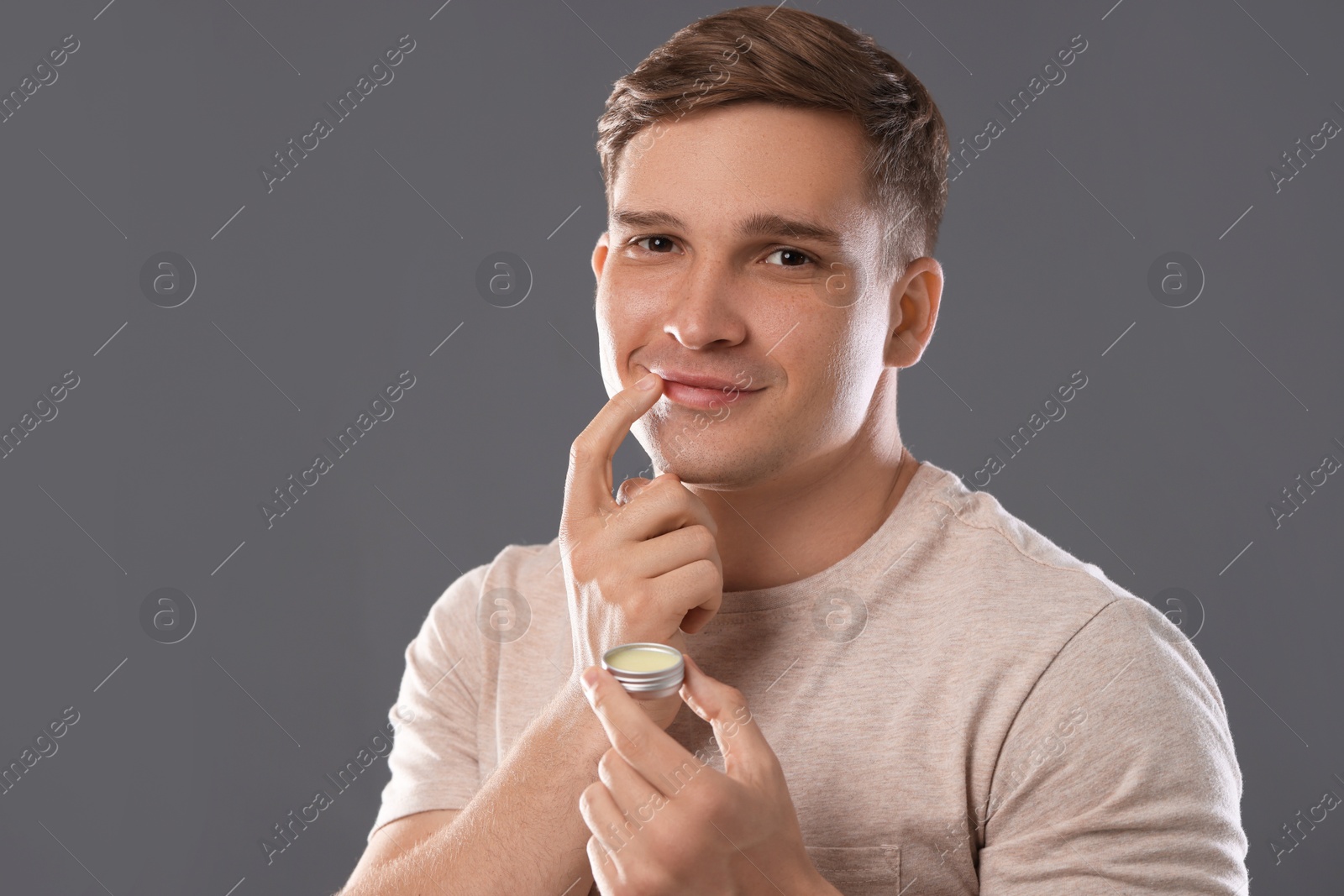 Young man applying lip balm onto his lips on grey background Photo of Young man applying lip balm onto his lips on grey background