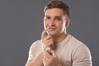 Photo of Young man applying lip balm onto his lips on grey background