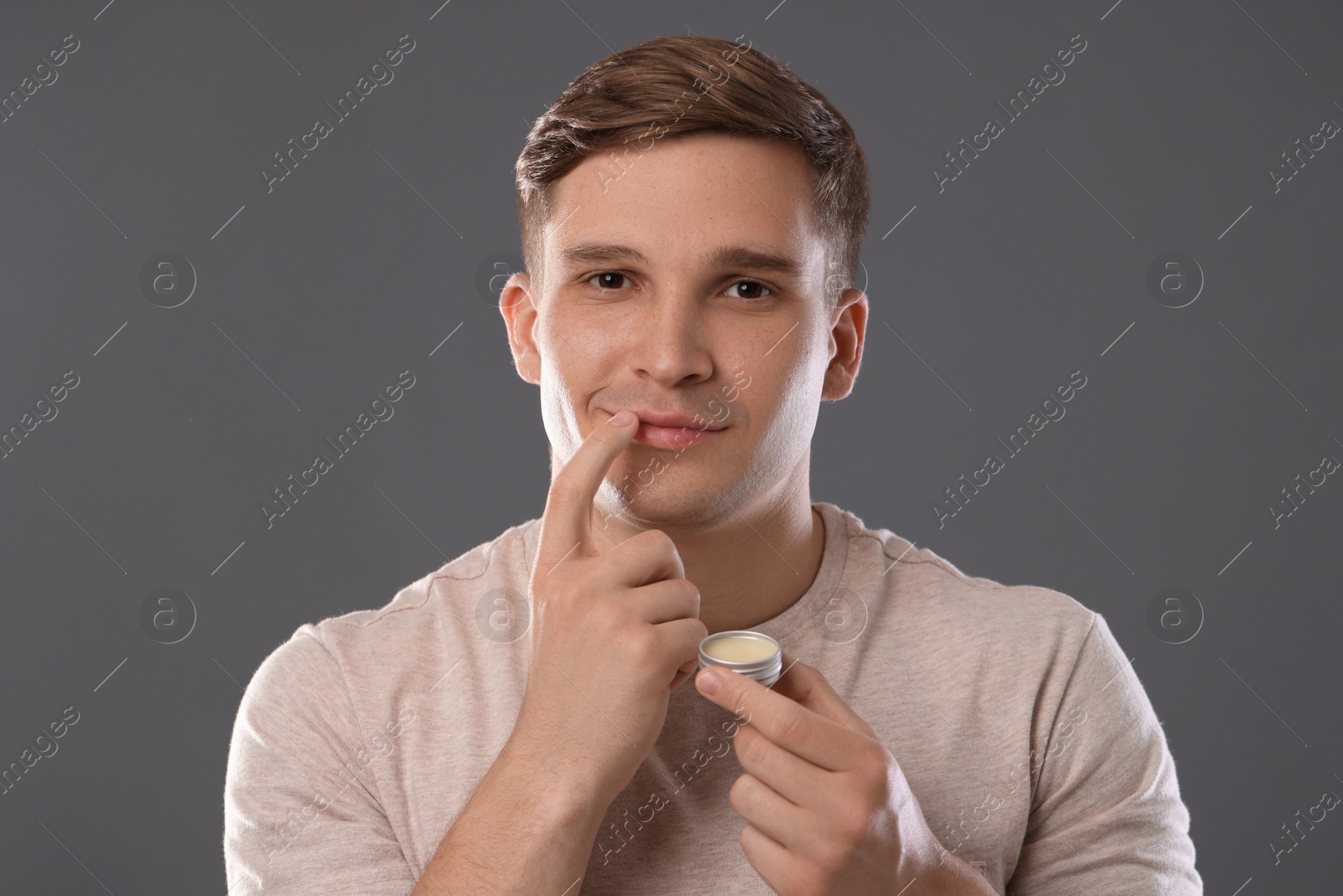 Young man applying lip balm onto his lips on grey background Photo of Young man applying lip balm onto his lips on grey background