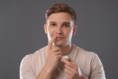 Photo of Young man applying lip balm onto his lips on grey background