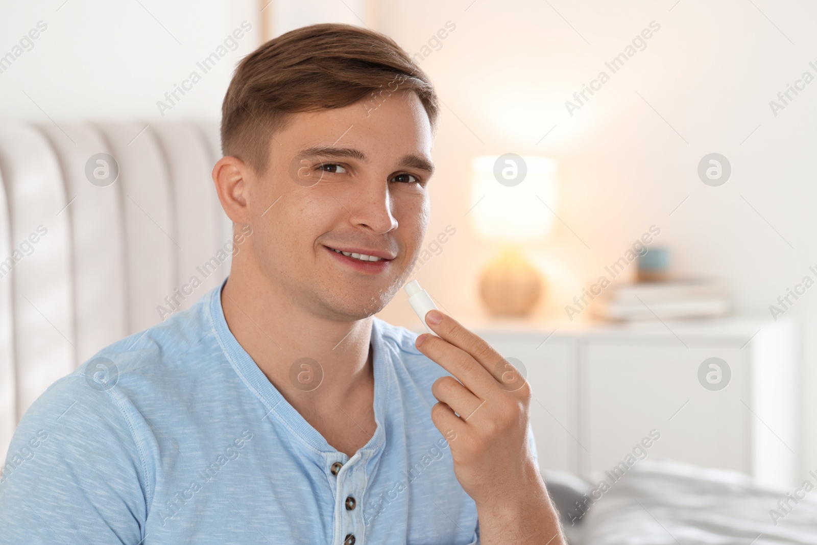 Young man applying lip balm onto his lips at home Photo of Young man applying lip balm onto his lips at home
