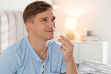 Photo of Young man applying lip balm onto his lips at home