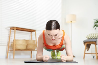 Photo of Young woman in sportswear doing plank exercise at home