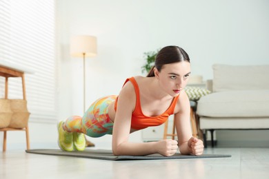 Photo of Young woman in sportswear doing plank exercise at home