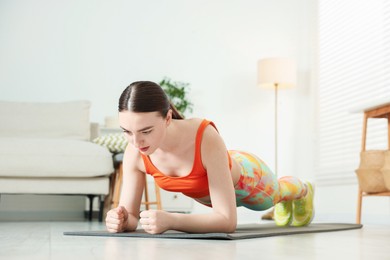 Photo of Young woman in sportswear doing plank exercise at home