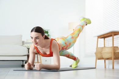 Photo of Young woman in sportswear doing plank exercise at home