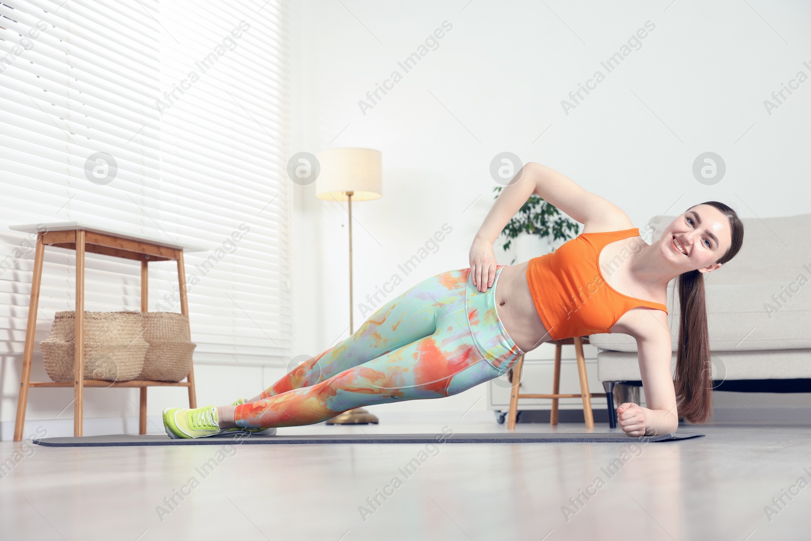 Smiling woman in sportswear doing side plank exercise at home Photo of Smiling woman in sportswear doing side plank exercise at home