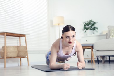 Photo of Young woman in sportswear doing plank exercise at home. Space for text
