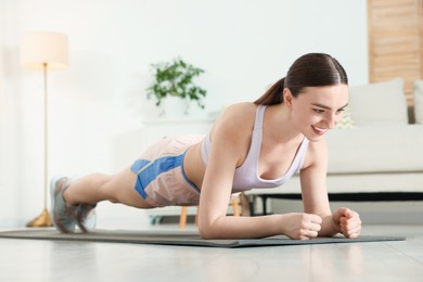 Photo of Smiling woman in sportswear doing plank exercise at home