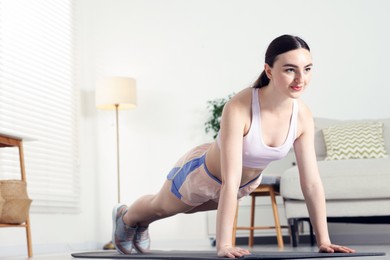 Photo of Young woman in sportswear doing plank exercise at home