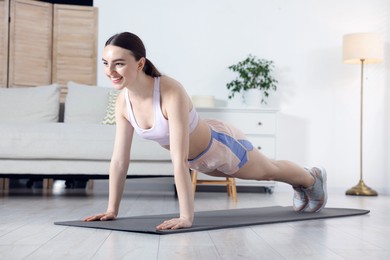 Photo of Smiling woman in sportswear doing plank exercise at home