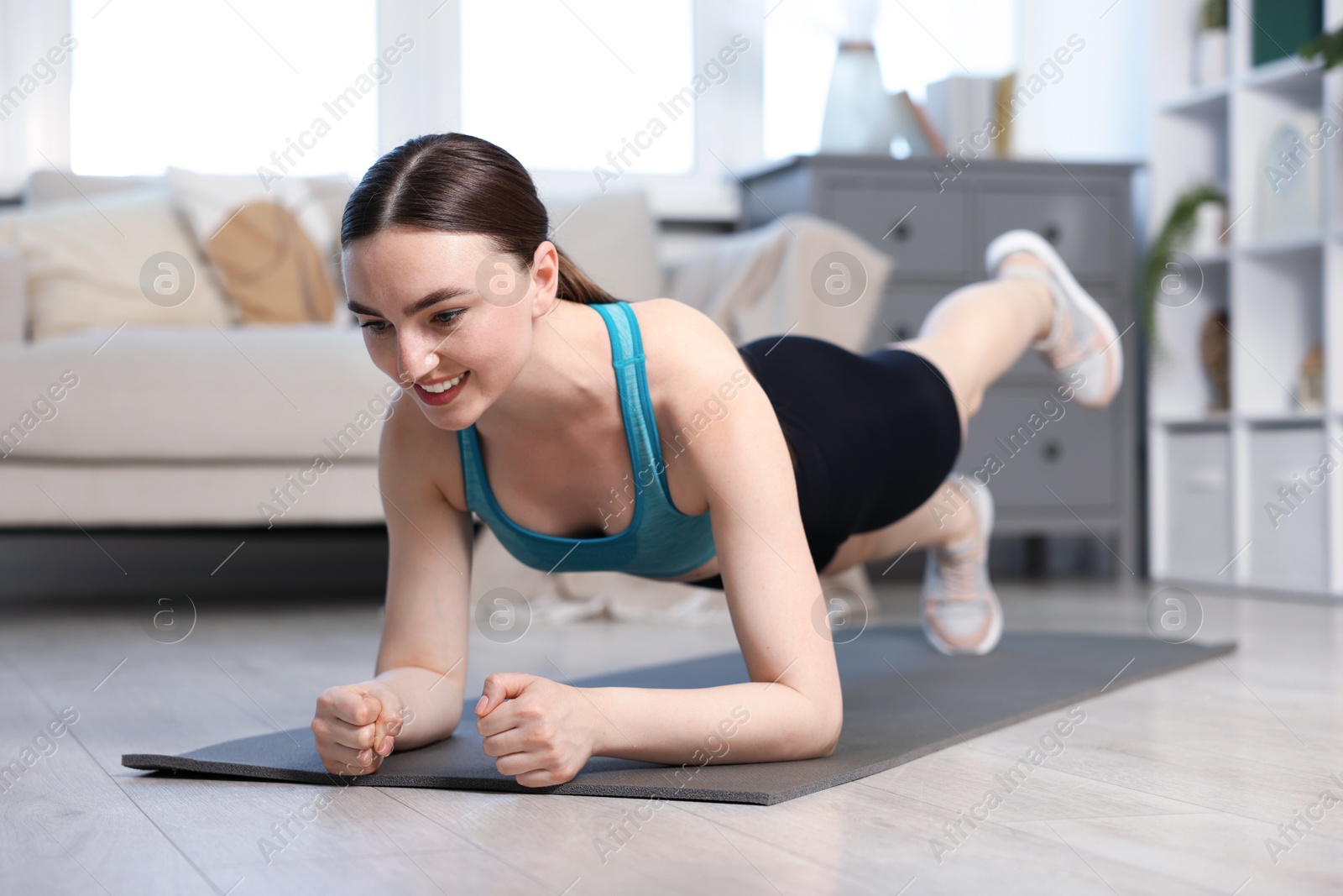 Smiling woman in sportswear doing plank exercise at home Photo of Smiling woman in sportswear doing plank exercise at home