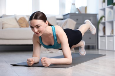 Photo of Smiling woman in sportswear doing plank exercise at home