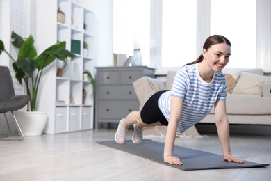 Photo of Smiling sporty woman doing plank exercise at home. Space for text