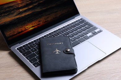 Photo of Passport and laptop on light wooden table, closeup