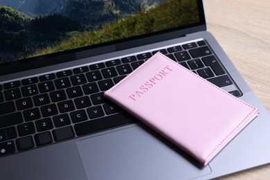 Photo of Passport and laptop on light wooden table, closeup