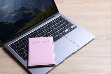 Photo of Passport and laptop on light wooden table, closeup