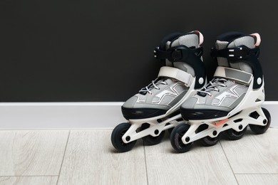 Photo of Pair of roller skates on floor near black wall, space for text