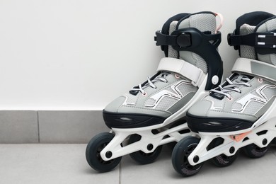 Photo of Pair of roller skates on floor near white wall, closeup. Space for text