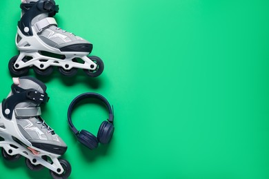Photo of Pair of roller skates and headphones on green background, top view. Space for text