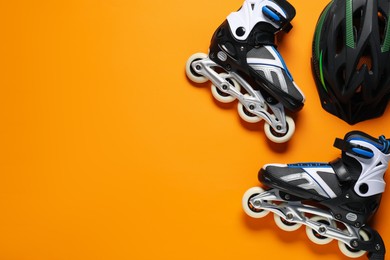 Photo of Pair of roller skates and helmet on orange background, top view. Space for text