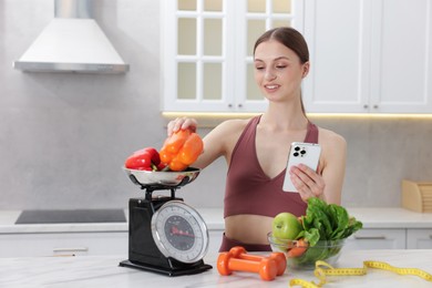 Photo of Woman with smartphone weighting bell peppers on kitchen scale at white marble table indoors