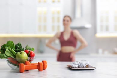 Photo of Slim woman in sportswear posing indoors, focus on kitchen scale, healthy food, dumbbells and measuring tape