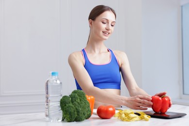 Photo of Woman weighting bell pepper on kitchen scale at white marble table indoors