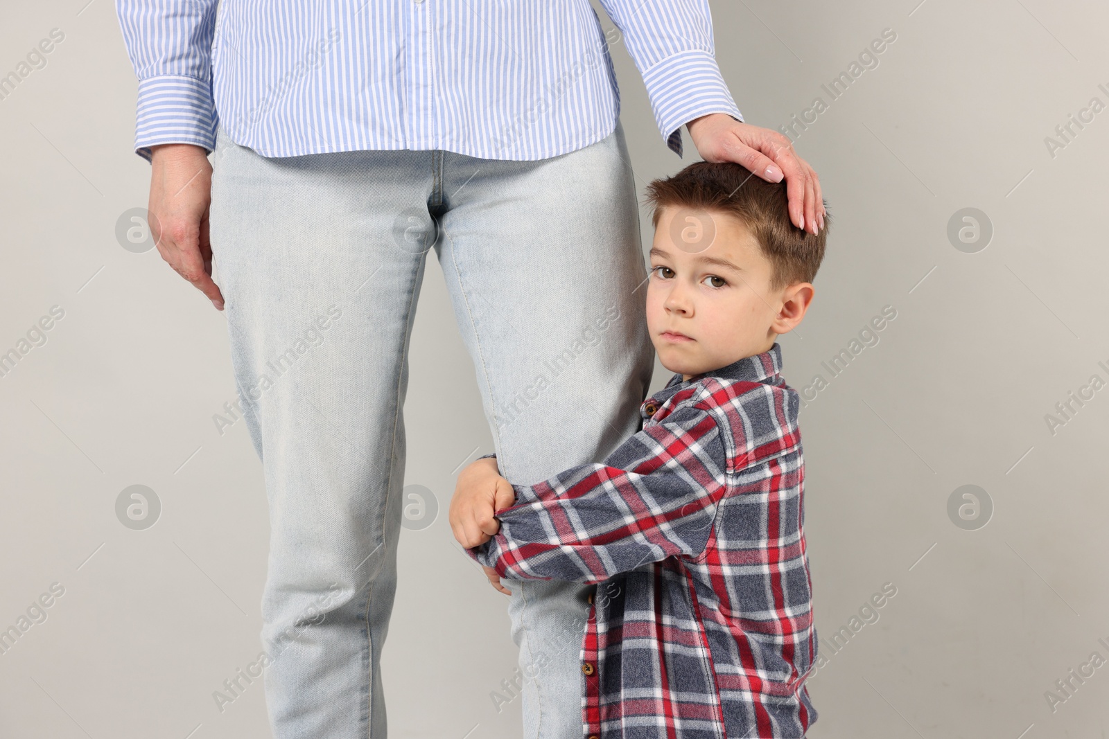 Little boy afraid to leave without mother and hugging her on grey background. Separation anxiety Photo of Little boy afraid to leave without mother and hugging her on grey background. Separation anxiety