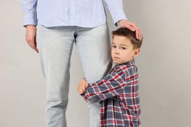 Photo of Little boy afraid to leave without mother and hugging her on grey background. Separation anxiety