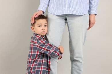 Photo of Little boy afraid to leave without mother and hugging her on grey background. Separation anxiety