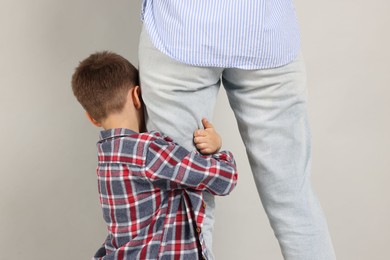 Photo of Little boy afraid to leave without mother and hugging her on grey background. Separation anxiety