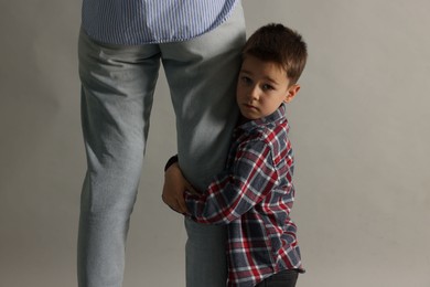 Photo of Little boy afraid to leave without mother and hugging her on grey background. Separation anxiety