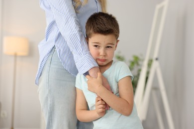 Photo of Little boy afraid to leave without mother and holding hands with her at home. Separation anxiety