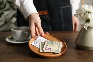 Photo of Waitress taking tips from wooden table in cafe, closeup