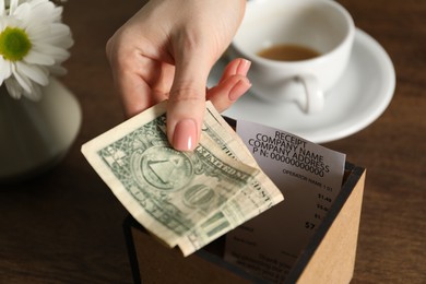 Photo of Woman putting tips into box at wooden table, closeup