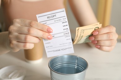Photo of Woman with receipt putting tips into metal bucket at white table in cafe, closeup