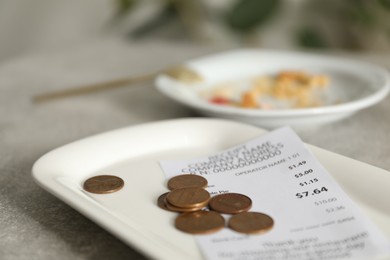 Photo of Tips, receipt and dirty plate on grey table in cafe, closeup