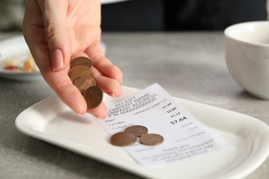 Photo of Woman putting tips onto plate at grey table in cafe, closeup
