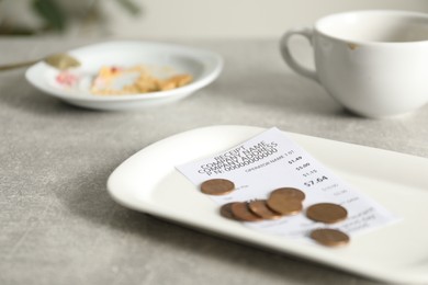 Photo of Tips, receipt, dirty plate and cup on grey table in cafe, closeup