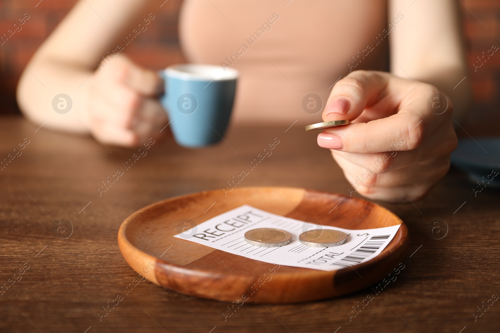 Woman putting tips onto plate at wooden table in cafe, closeup Photo of Woman putting tips onto plate at wooden table in cafe, closeup