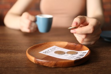 Photo of Woman putting tips onto plate at wooden table in cafe, closeup