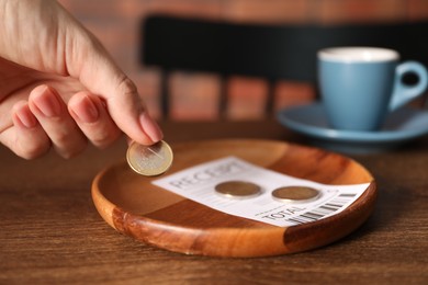 Photo of Woman putting tips onto plate at wooden table in cafe, closeup